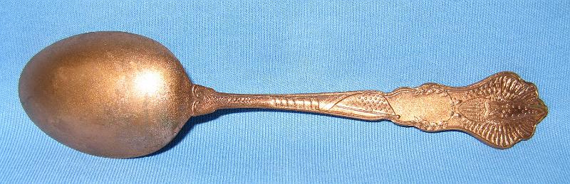 C & A Shaft Reverse.JPG - SOUVENIR MINING SPOON C & A SHAFT BISBEE ARIZONA - Copper souvenir spoon, circa 1900, embossed mining scene in bowl with C. and A. Shaft above and Bisbee, Ariz. below, handle finial with Arizona territorial seal and ARIZONA on the handle, fancy design on handle reverse, 5 1/4 in. long [Although Phelps Dodge, owner and operator of the famous Copper Queen mine, was the largest mining company in Bisbee, Arizona it was not the only one. The Calumet and Arizona (C&A) Mining Company, organized in March 1901 with Charles Briggs as president, operated several large and profitable mines, principal among them the Irish Mag mine, adjacent to the Copper Queen.  By 1907, the C&A was the fourth-most productive copper mine in Arizona, and ran its own smelter in Douglas, Arizona. In 1911, the company merged with the Superior and Pittsburg Copper Company ultimately buying out Superior and Pittsburg in 1915.  The original C&A mine included 12 claims and 178 patented acres adjoining the Copper Queen.  With John C. Greenway as general manager, the company expanded operations to include the Irish Mag shaft to a depth of 1350 feet, the Ontario shaft to a depth of 1450 feet, the Powell shaft to 600 feet deep, the Hoatson shaft to 1530 feet deep and the Junction shaft to 1837 feet deep.  By 1910 the C&A employed 1274 men, 805 at the mine and 469 at the smelter.  In 1915 copper production exceeded 65 million pounds and by 1916, the company controlled over 2000 acres of mining property within the Warren Mining District.  The C&A was the first mine in Arizona to discontinue work on Sundays effective August 1910. The company’s fortunes took a turn for the worse in the 1920s and with the company failing, Phelps Dodge bought out their old nemesis in September 1931.]  
